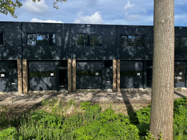 Moderne bedrijfsunits aan de Broekdijk West met zwarte gevels en grote ramen, omringd door groen.